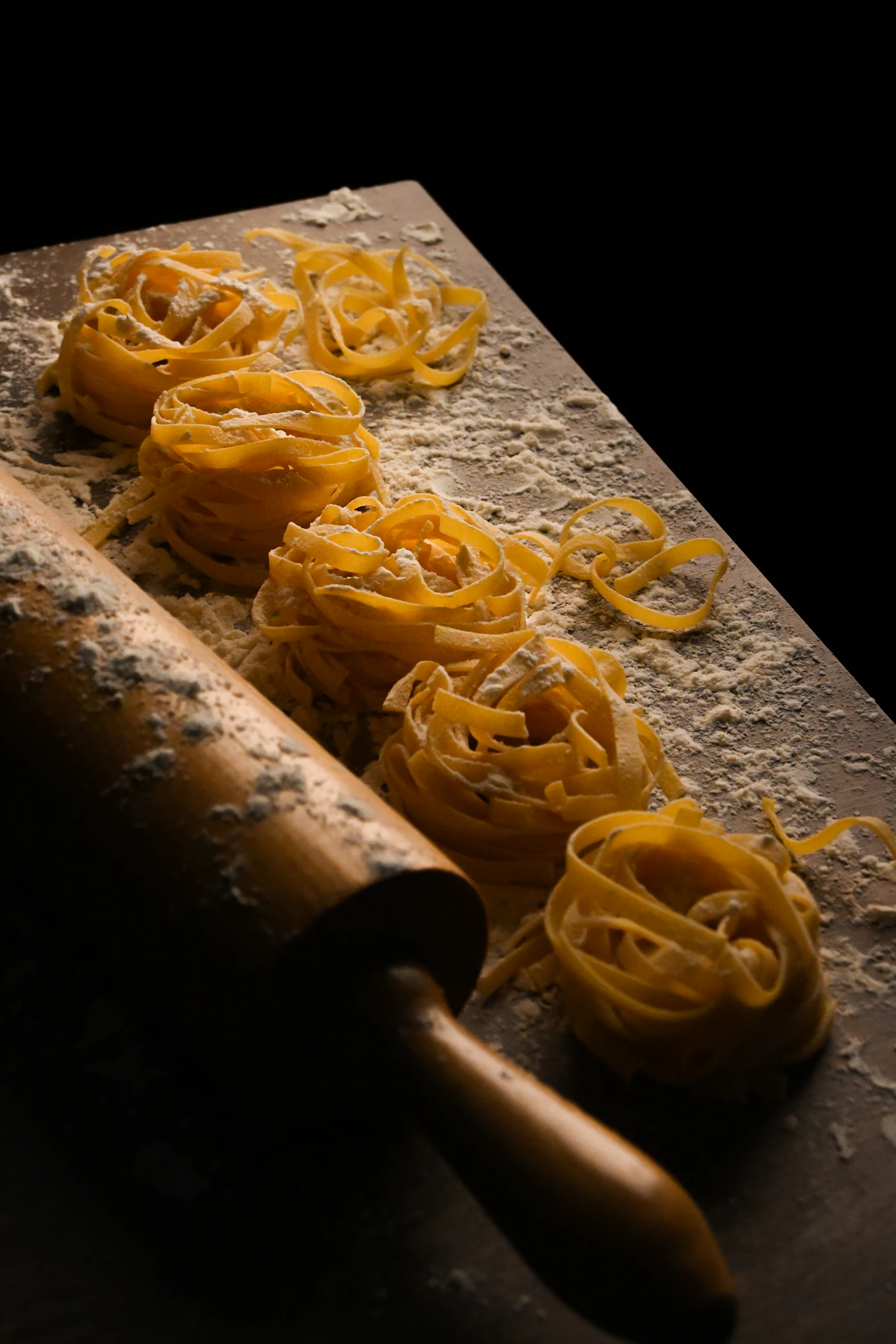 Frische Tagliatelle-Nester mit Nudelholz und Mehl